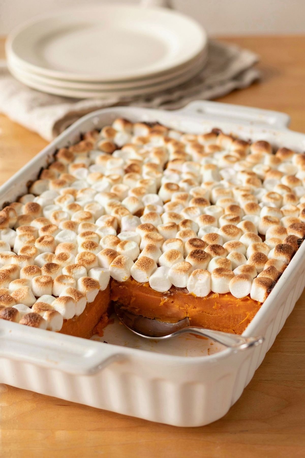 Sweet potato casserole in a white baking dish, deep orange baked sweet potato under a layer of golden toasted mini marshmallows, with one serving scooped out to show the set layers