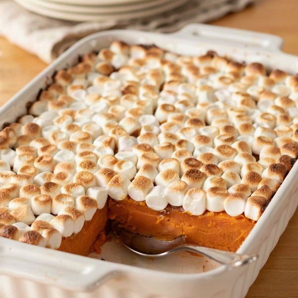 Sweet potato casserole in a white baking dish, deep orange baked sweet potato under a layer of golden toasted mini marshmallows, with one serving scooped out to show the set layers