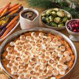 A vegetarian Thanksgiving table with sweet potato casserole under toasted marshmallows, a jug of mushroom gravy, roasted Brussels sprouts, cranberry sauce and roasted rainbow carrots.