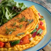Golden vegan omelette with fresh spinach, tomatoes, and bell peppers garnished with herbs.