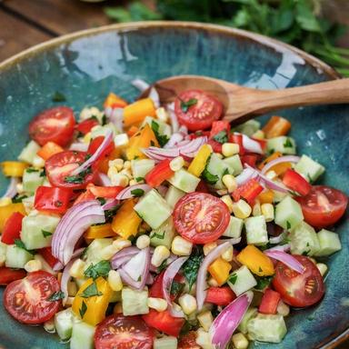 Chopped veggie salad without lettuce in a teal bowl: halved cherry tomatoes, diced cucumber, red, yellow and orange bell pepper, sweetcorn, thin pink red onion and parsley glossy with lemon and olive oil dressing.