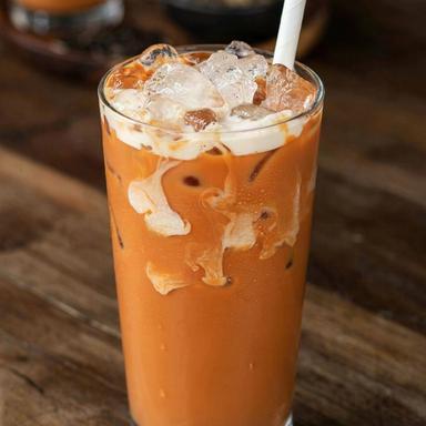 A tall glass of Thai iced tea, bright orange milk tea over ice with evaporated milk drifting down from the top in white clouds and a paper straw.