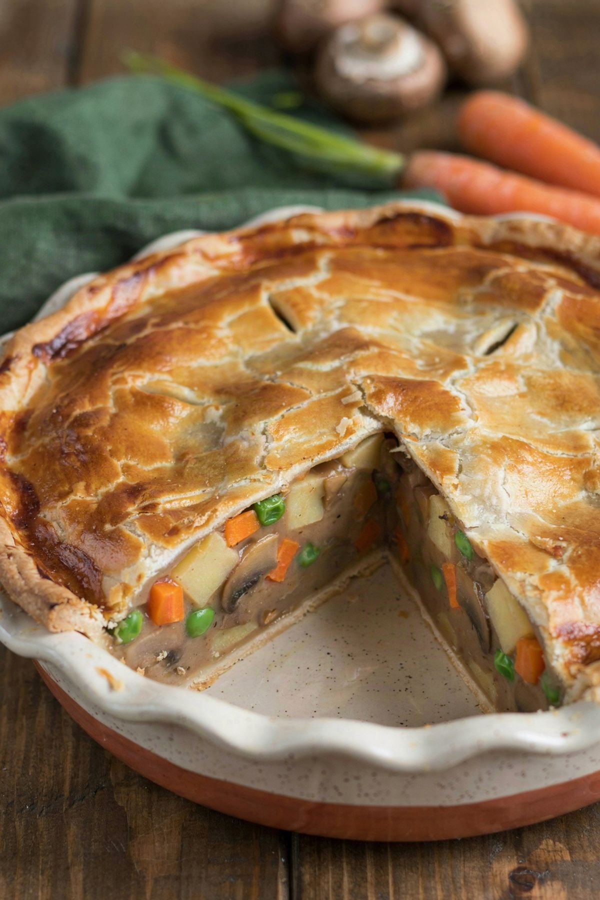 Vegetarian pot pie in a white speckled ceramic dish with one wedge cut out, the filling standing firm at the cut face with potato, carrot, browned mushrooms and peas in a thick beige gravy under a golden pastry crust