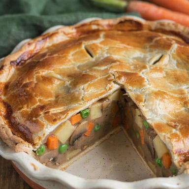 Vegetarian pot pie in a white speckled ceramic dish with one wedge cut out, the filling standing firm at the cut face with potato, carrot, browned mushrooms and peas in a thick beige gravy under a golden pastry crust