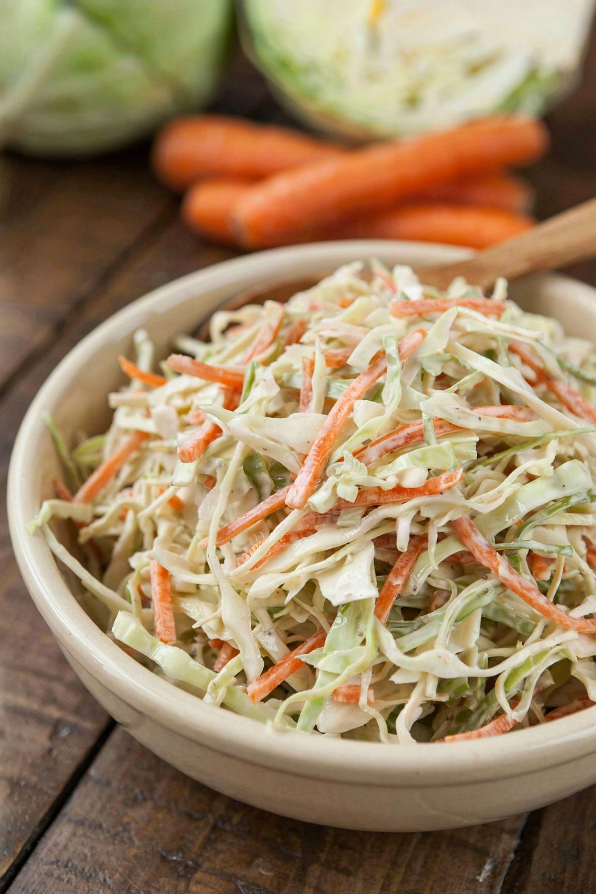 Vegan cole slaw in a cream stoneware bowl, finely shredded green cabbage and grated carrot lightly coated in creamy ivory dressing