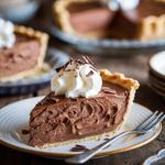 A slice of silken chocolate cream pie with whipped cream and chocolate shavings on a plate.
