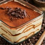Layered vegan tiramisu with cream, cocoa, and chocolate shavings, topped with coffee beans.