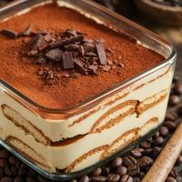Layered vegan tiramisu with cream, cocoa, and chocolate shavings, topped with coffee beans.