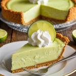 A slice of vegan key lime pie with creamy filling and graham cracker crust, garnished with lime and whipped cream.