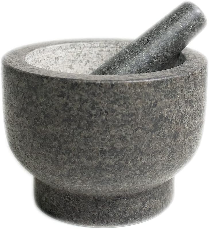 A deep gray granite mortar with a pale unpolished interior and a footed base, with its granite pestle resting inside.