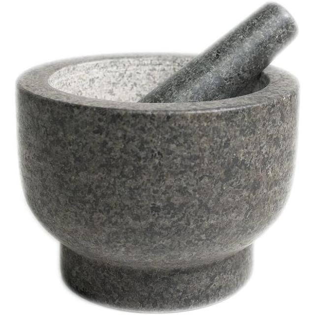 A deep gray granite mortar with a pale unpolished interior and a footed base, with its granite pestle resting inside.
