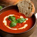 A bowl of creamy vegan tomato soup garnished with basil, served with crusty bread on a wooden table.