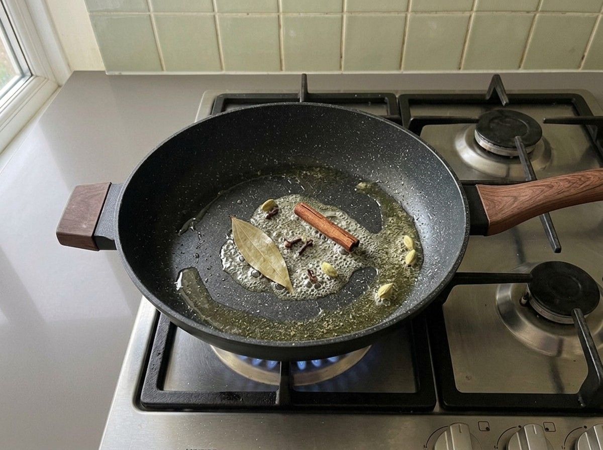 Bay leaf, cinnamon stick, cloves and green cardamom pods sizzling in melted ghee in a skillet