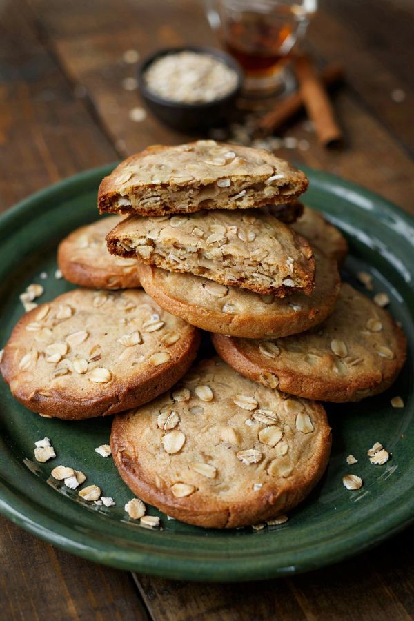 Vegan oatmeal cookies stacked on a green stoneware plate, thick golden discs packed with rolled oats, one broken open to show the chewy inside