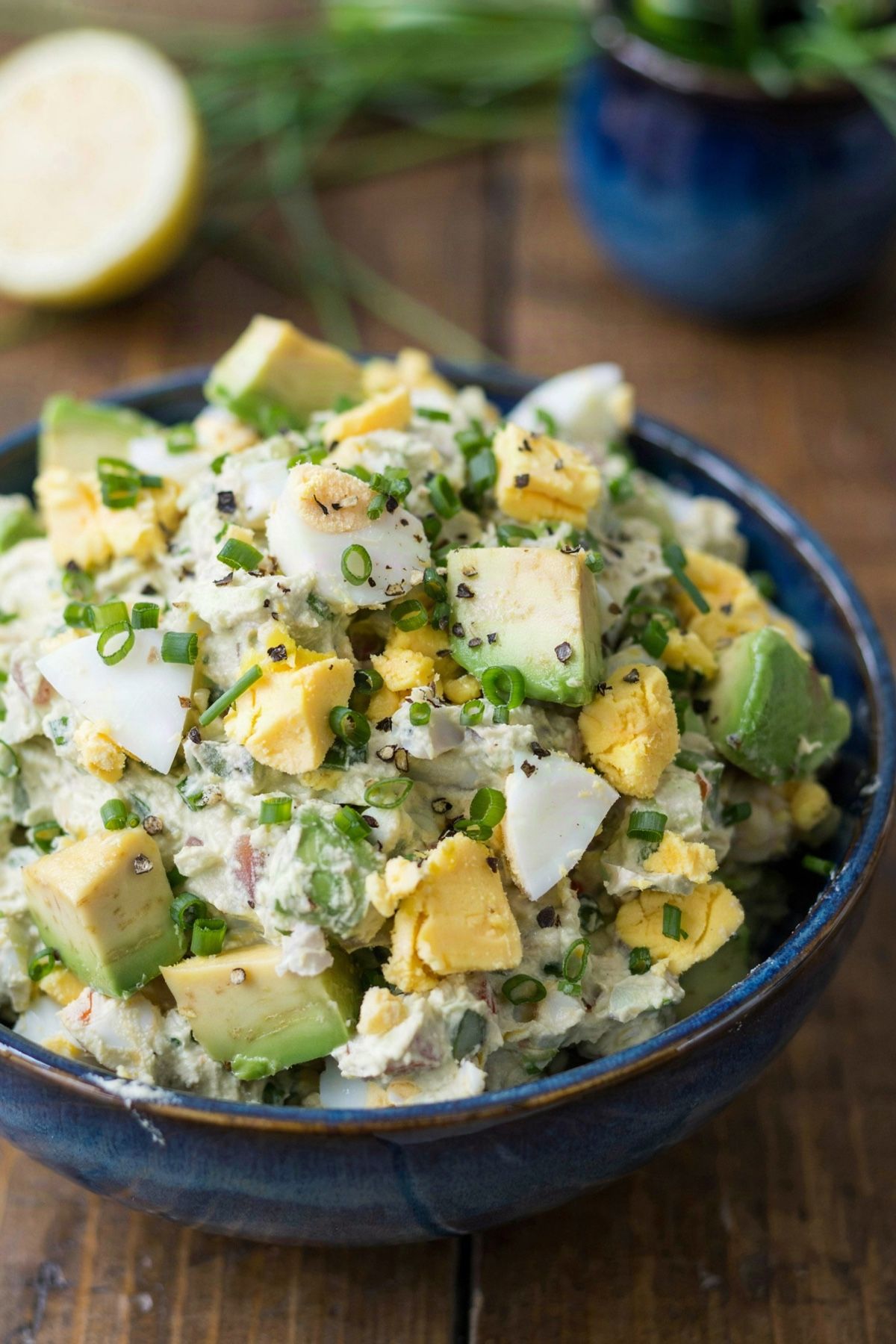 Avocado egg salad in a deep blue bowl, chunks of green avocado and pieces of hard-boiled egg folded through a creamy pale green base with chives and cracked black pepper.