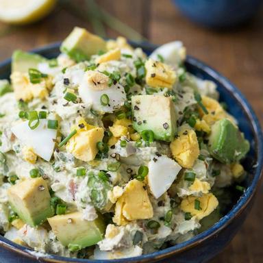 Avocado egg salad in a deep blue bowl, chunks of green avocado and pieces of hard-boiled egg folded through a creamy pale green base with chives and cracked black pepper.