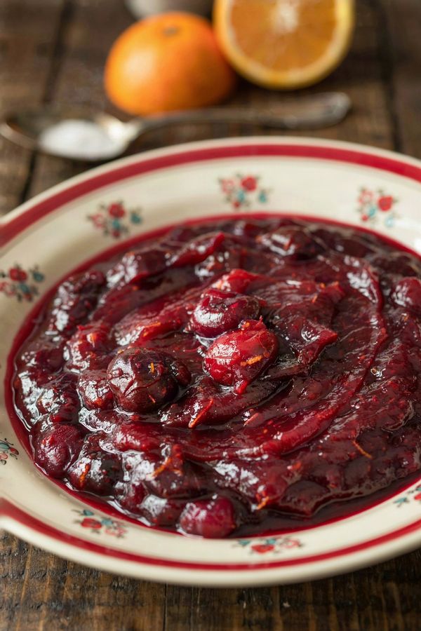 Cranberry orange sauce set thick in a cream floral bowl, dark crimson and glossy with burst berries and flecks of orange zest