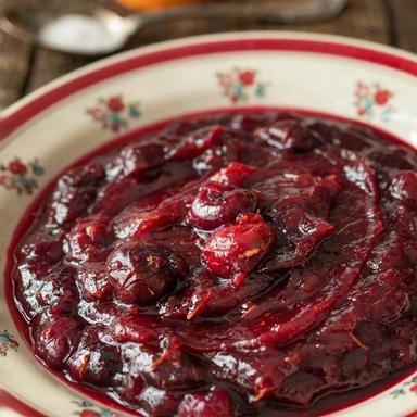 Cranberry orange sauce set thick in a cream floral bowl, dark crimson and glossy with burst berries and flecks of orange zest