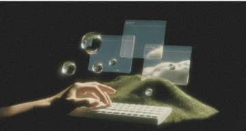 A hand types on a keyboard on a grassy mound, surrounded by floating translucent windows and reflective bubbles.