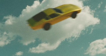 Yellow car flying in a blue sky with clouds.