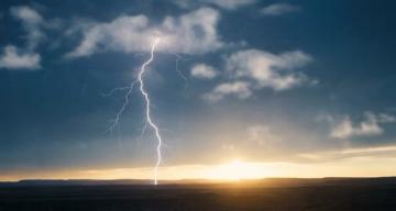 Lightning striking the ground under stormy clouds with a sunset on the horizon.