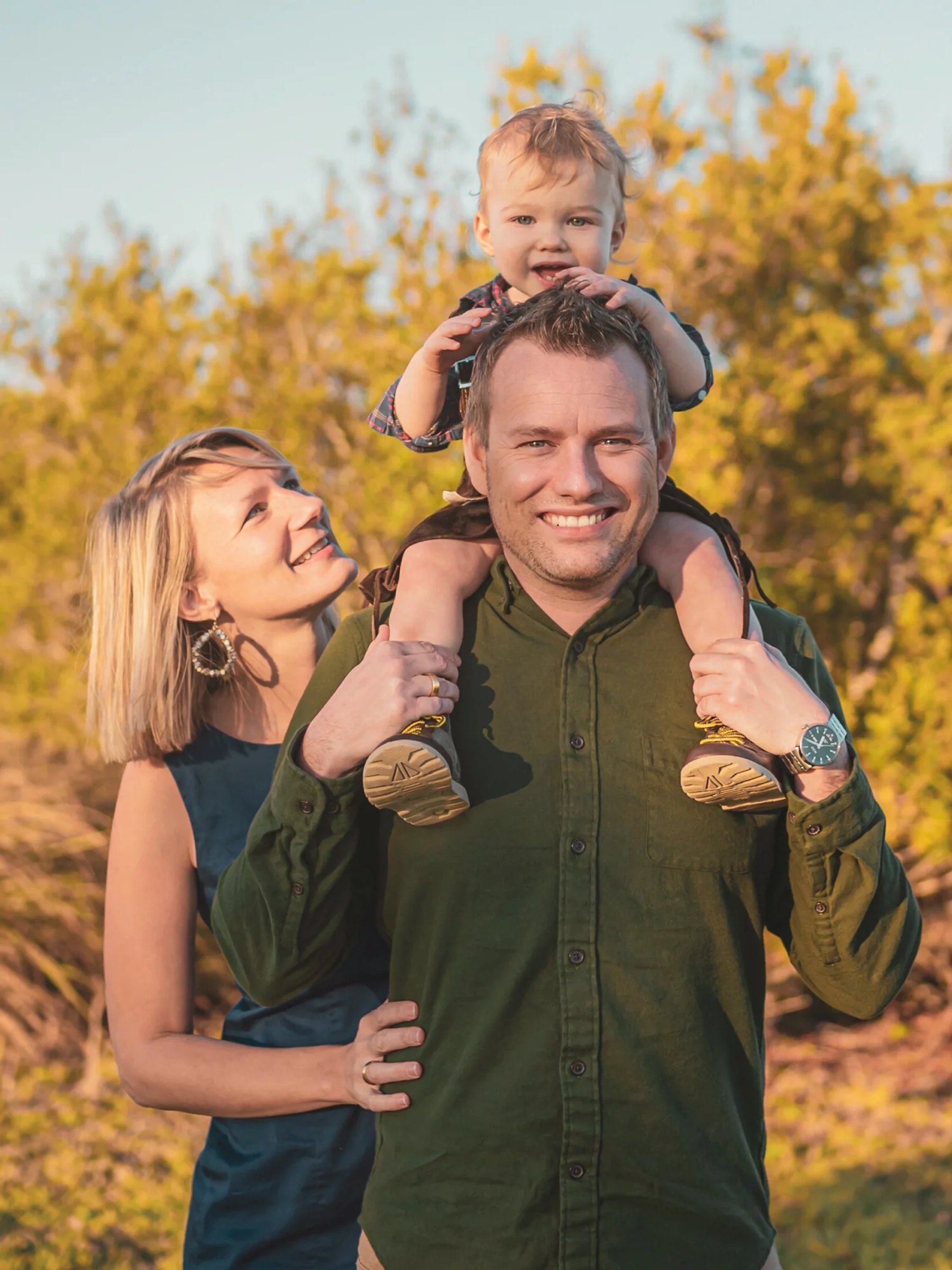 Parents smiling with their child on his father’s shoulders