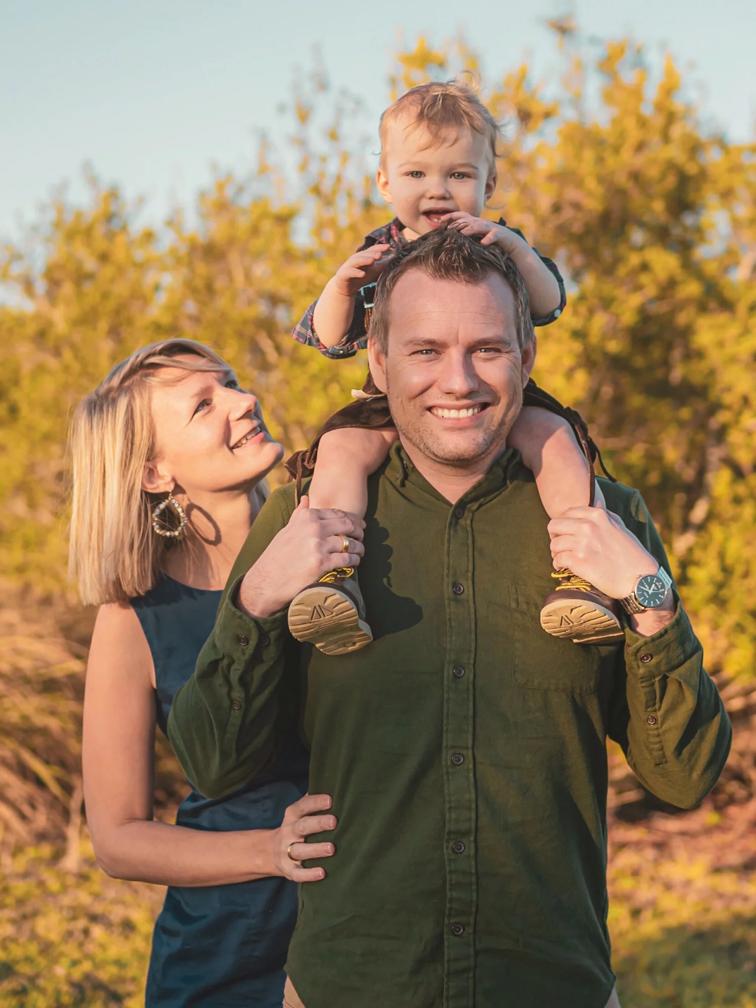 Parents smiling with their child on his father’s shoulders