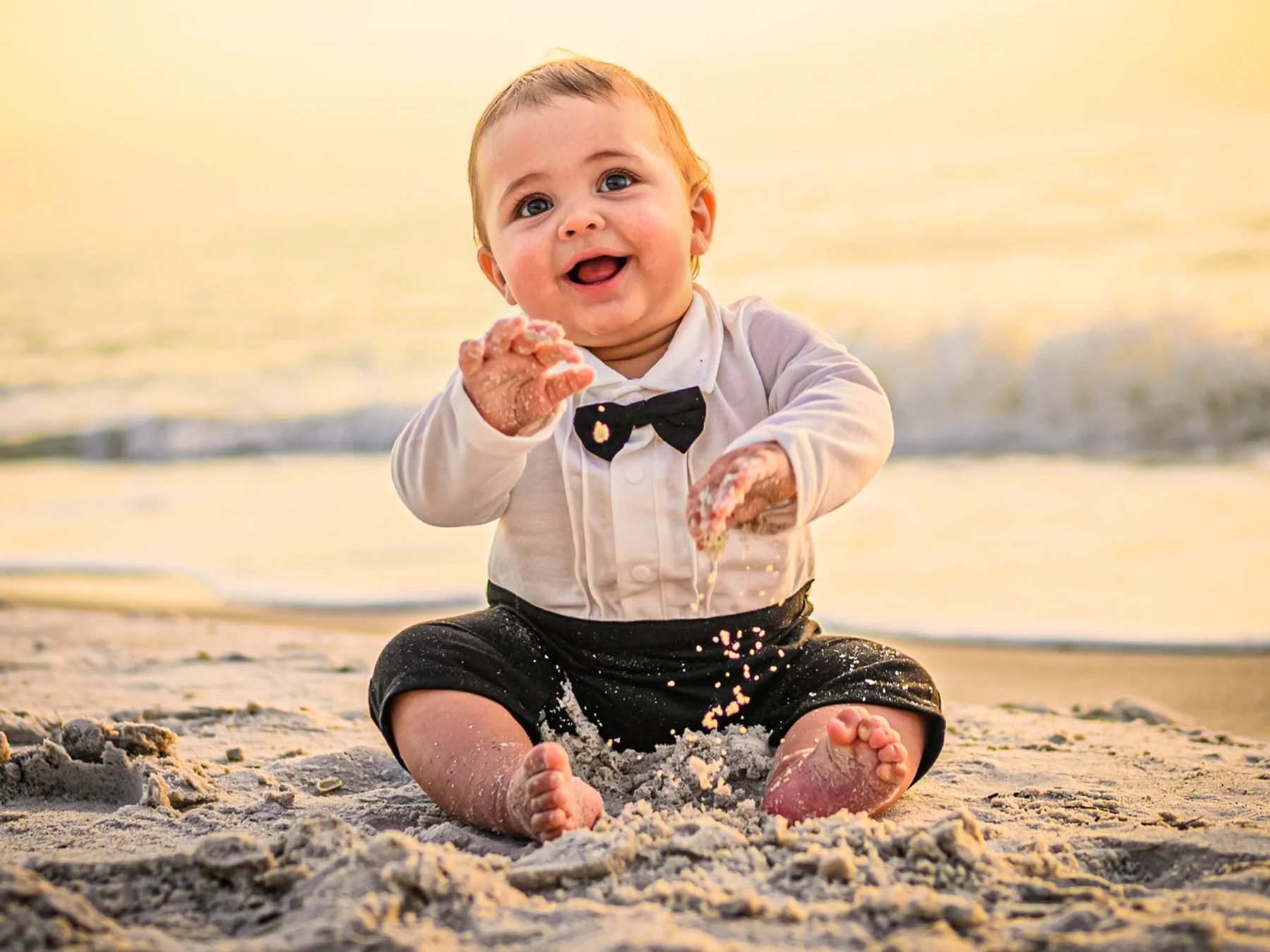 A baby sitting on the beach at sunset