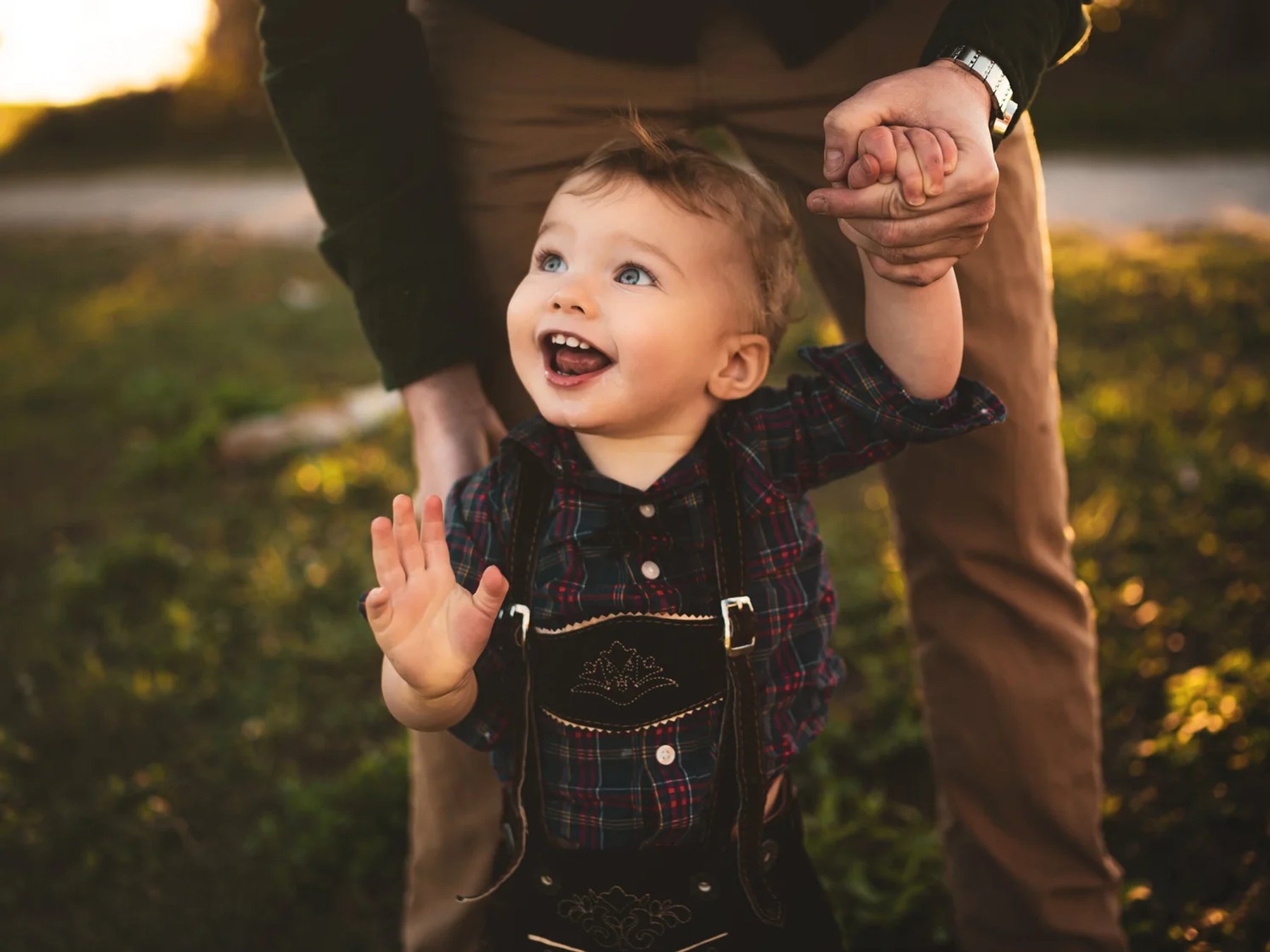 A young child smiling up at her father while holding his hand