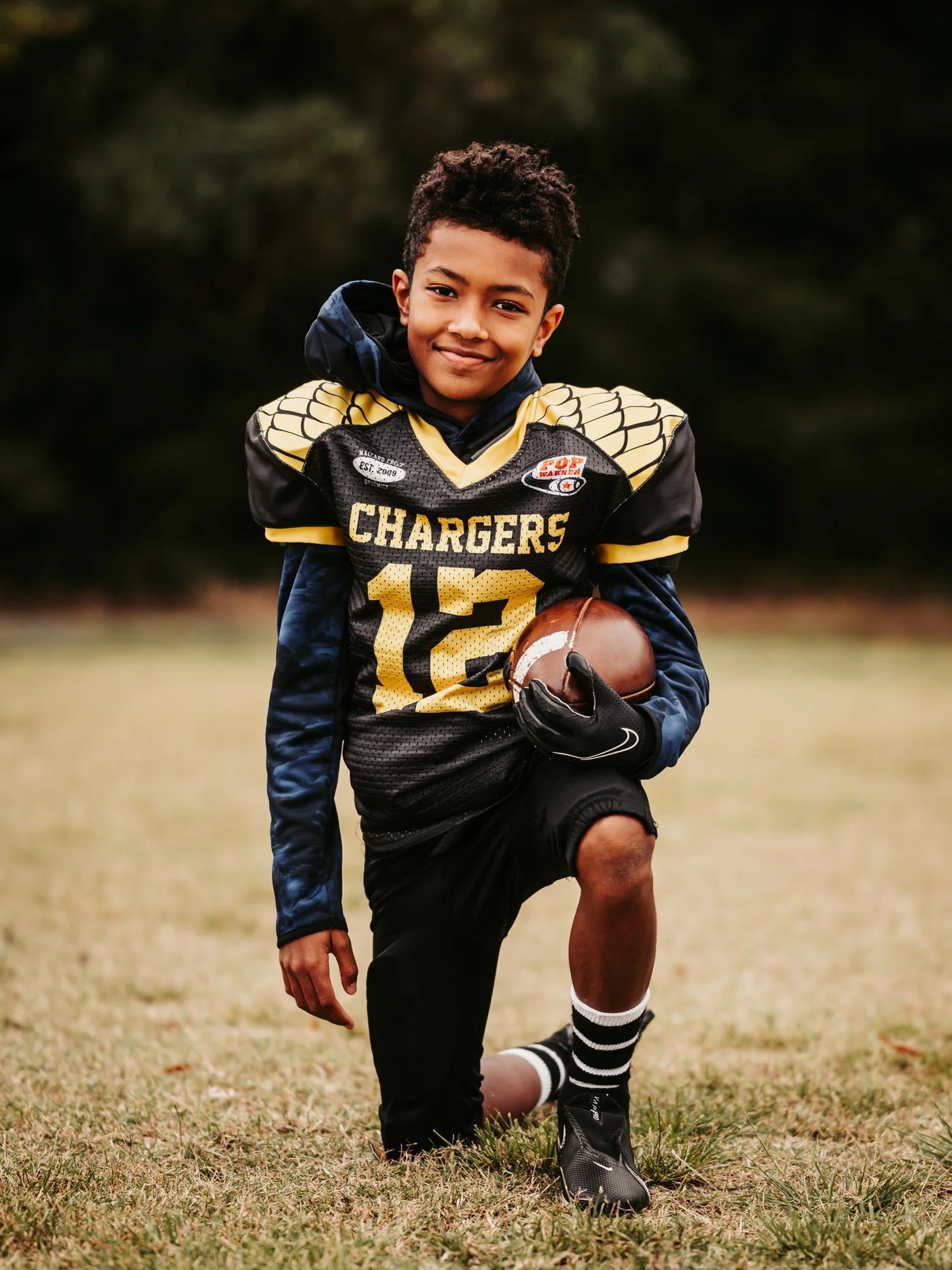 A young football player holding a football in his team uniform
