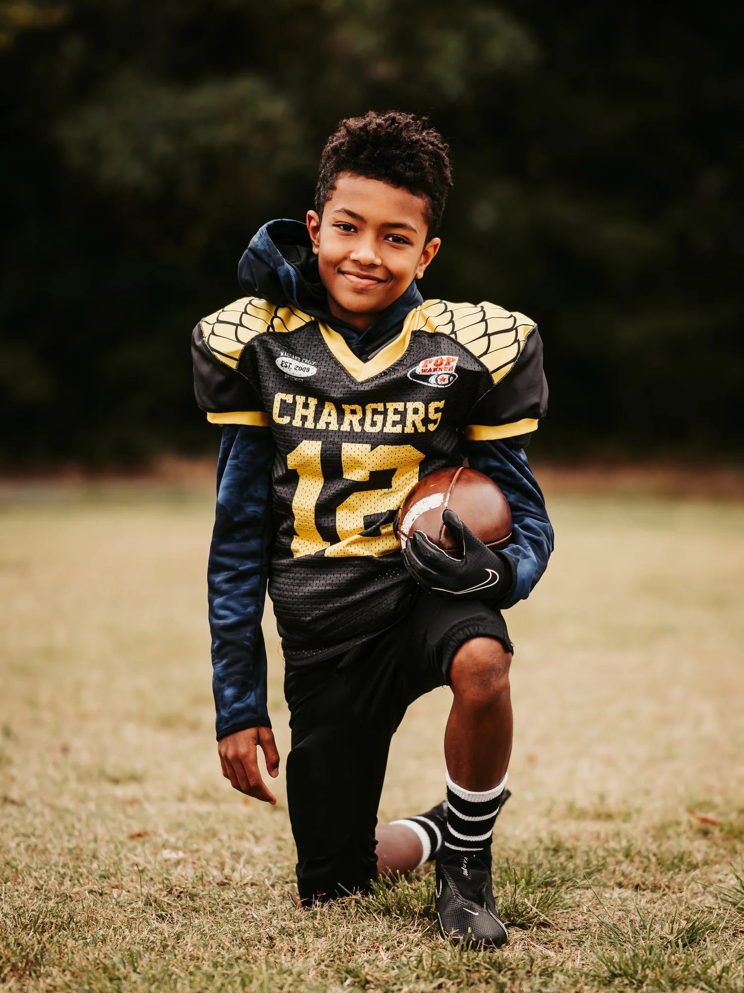 A young football player holding a football in his team uniform