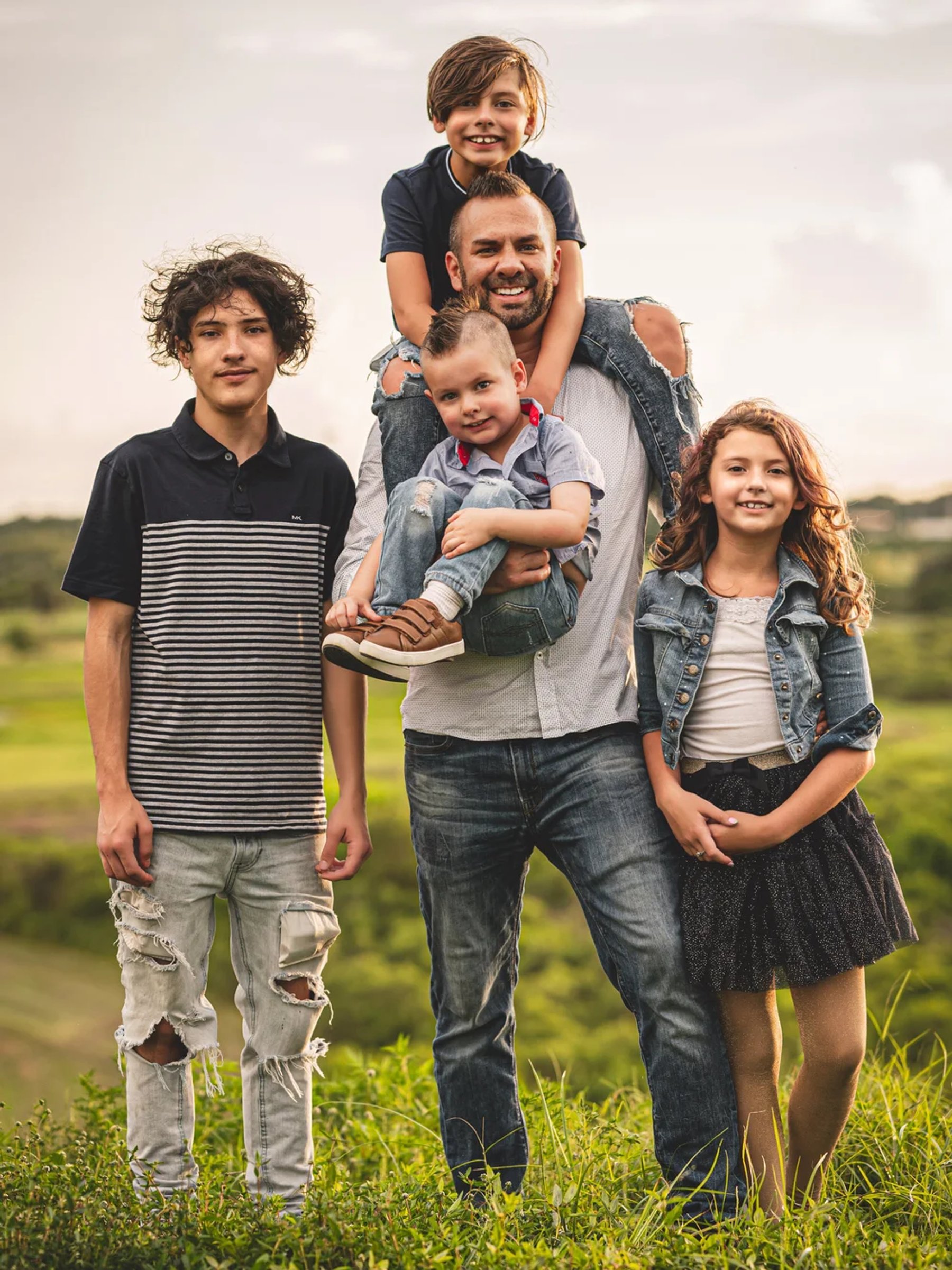 Five-person outdoor portrait, with one child on a man's shoulders and another in his arms.