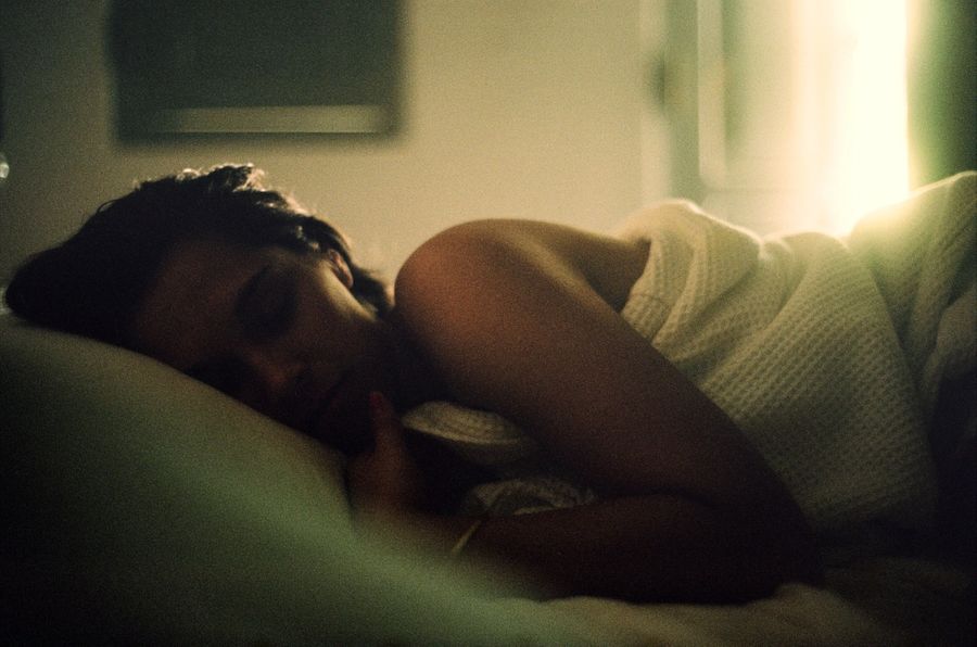 A woman lies on the bed dreaming as the sun pours in through the window behind her.
