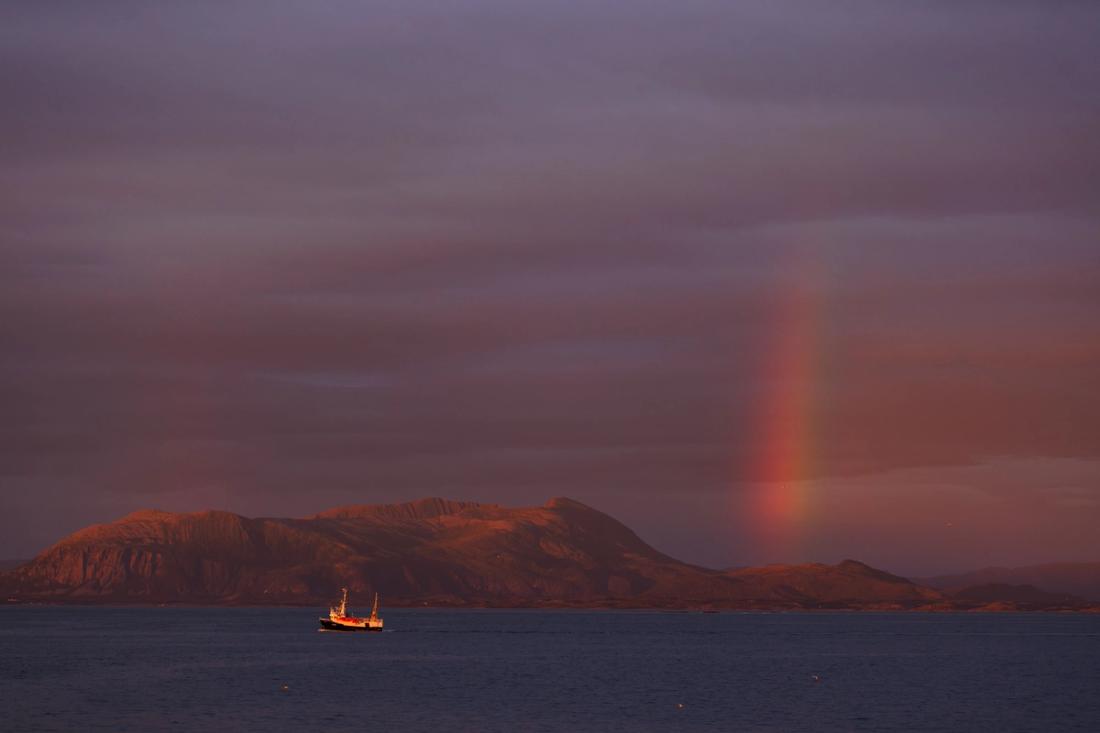 A boat on calm water with a rainbow behind it.