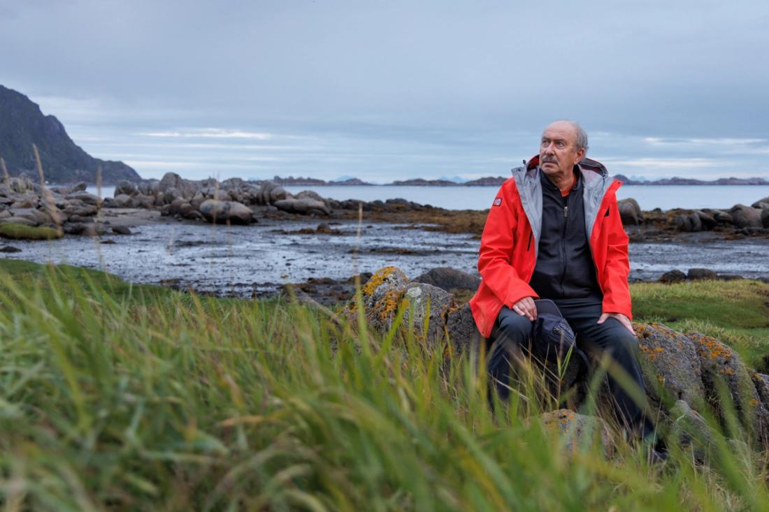 Senior scientist Hartvig Christie sitting on a rock with a fjord visible behind him.
