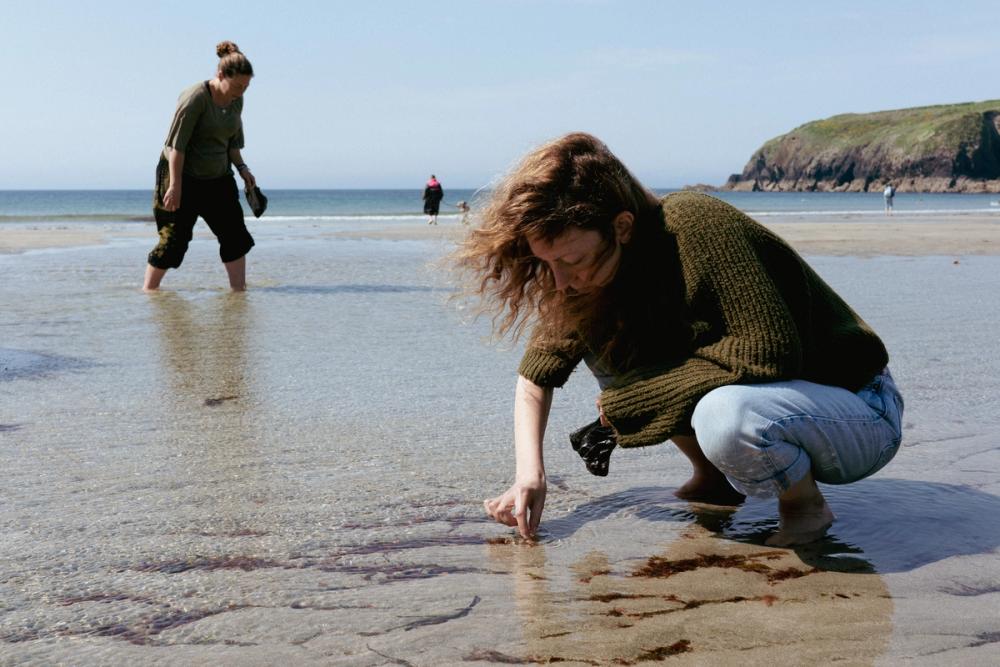 Woman crouching on the beach collecting seaweed.