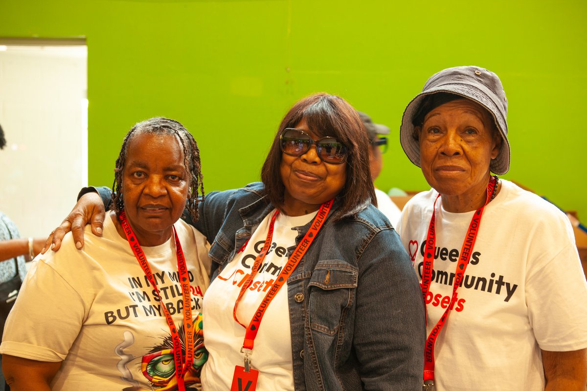 Three Queens Community Closets volunteers in matching t-shirts smiling together at the resource fair
