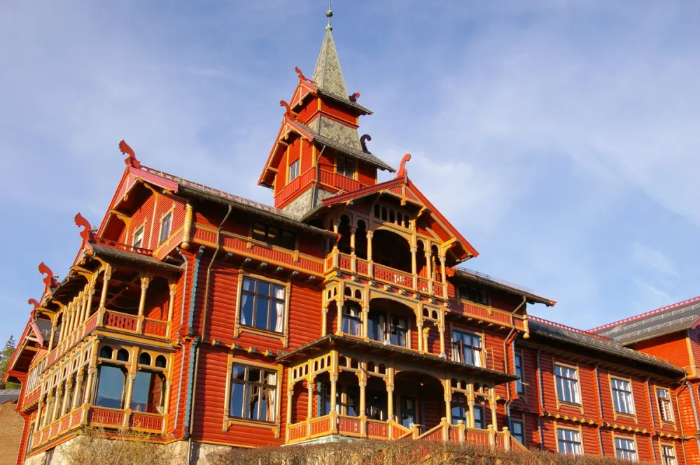 Exterior of the Scandic Holmenkollen Park Hotel in Oslo, showing its red wooden façade, ornate carvings and dragon-style architectural details.