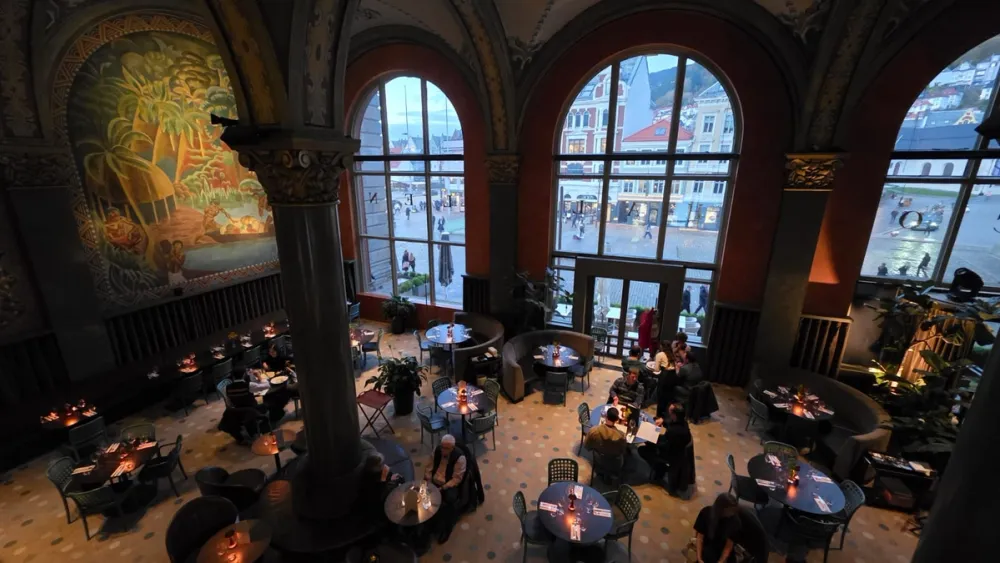 Interior of Frescohallen in Bergen, showing candlelit tables beneath tall arched windows and colorful frescoes on the walls. Once a historic bank building, it now serves as a restaurant blending art, history, and modern dining.