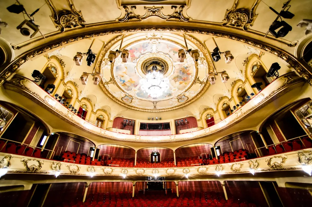 Interior of the National Theatre’s main auditorium in Oslo, with ornate gold detailing, red seats, and a painted ceiling.