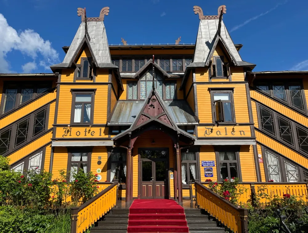 Front entrance of the yellow wooden Dalen Hotel in Telemark, Norway, with dragon-head roof ornaments and red-carpeted stairs.