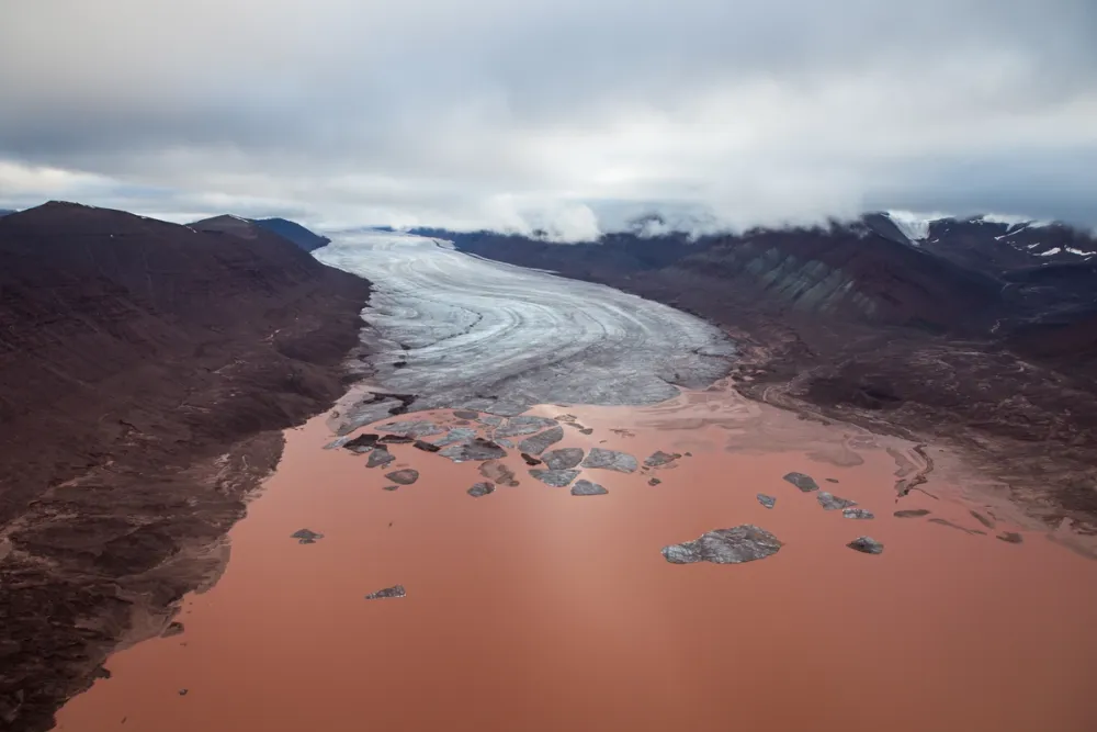 A surreal red glacial lake in the Arctic, flanked by stark mountains and sweeping ice flows. Svalbard’s geological variety offers otherworldly backdrops, often used in major film productions to represent uncharted or alien landscapes.