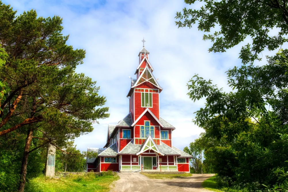 The historic Buksnes Church in Gravdal, Lofoten, featuring red wooden cladding and carved dragon-style details.