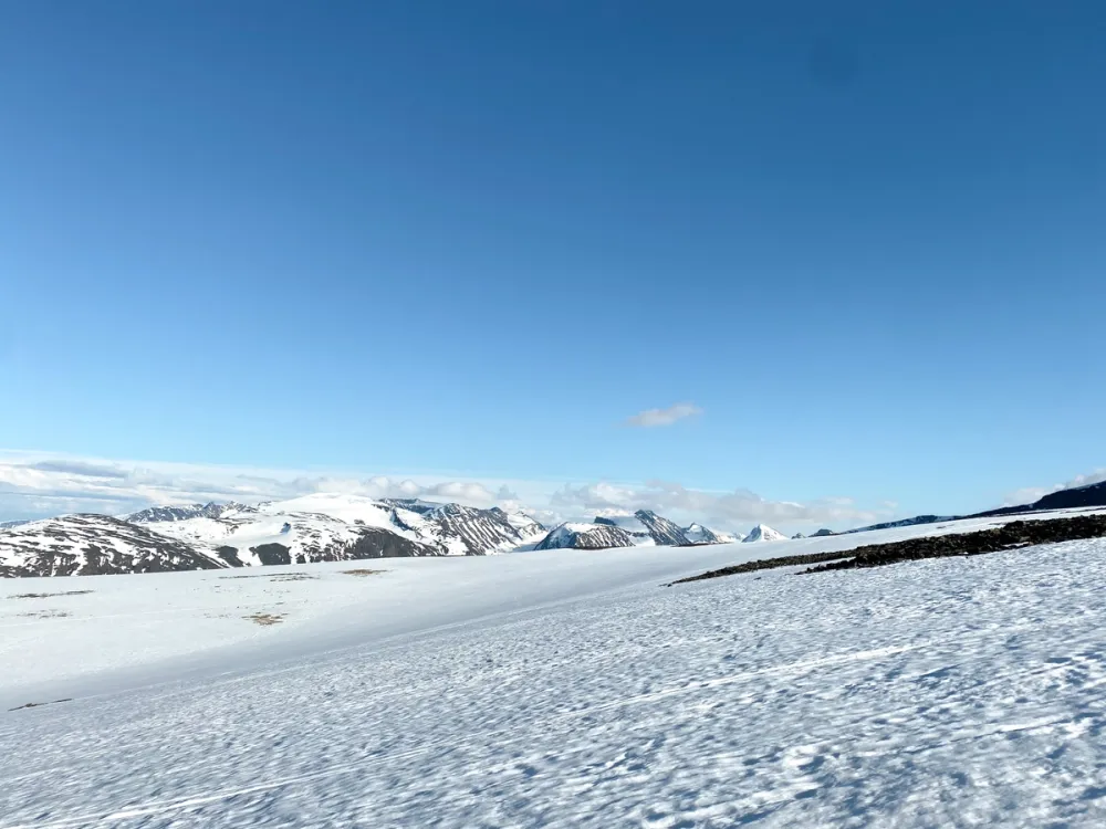 Snow-covered landscape at Galdhøpiggen Summer Ski Centre in Jotunheimen, Norway, with surrounding mountains and clear blue sky.