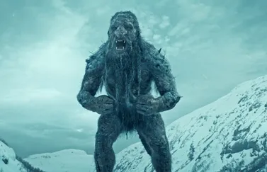 A giant troll with a rugged, rock-covered body stands roaring in a snowy mountain valley, surrounded by dramatic winter scenery in Jotunheimen from Troll 2.