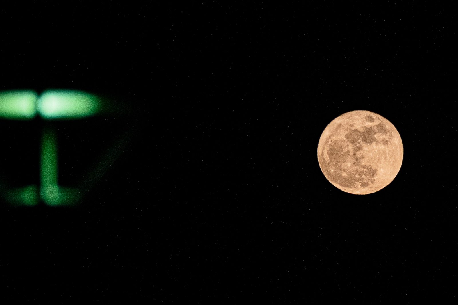 A full moon with visible craters appears on the right side of a night sky filled with stars, while a green traffic light glows on the left against the black background.