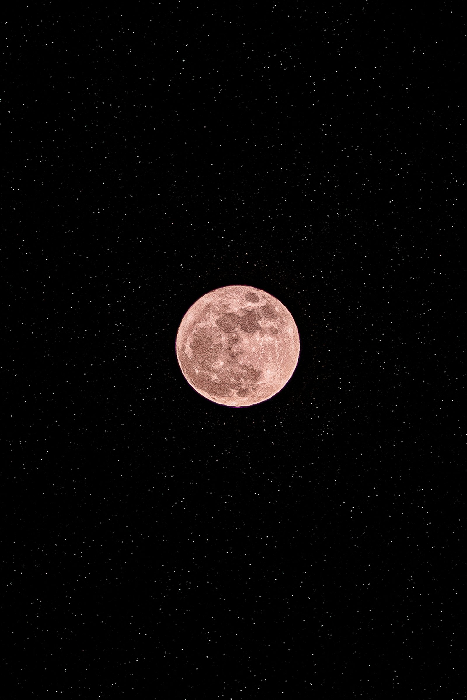 A full moon with visible craters rendered in soft pink and peach tones centered against a black sky filled with scattered white stars.