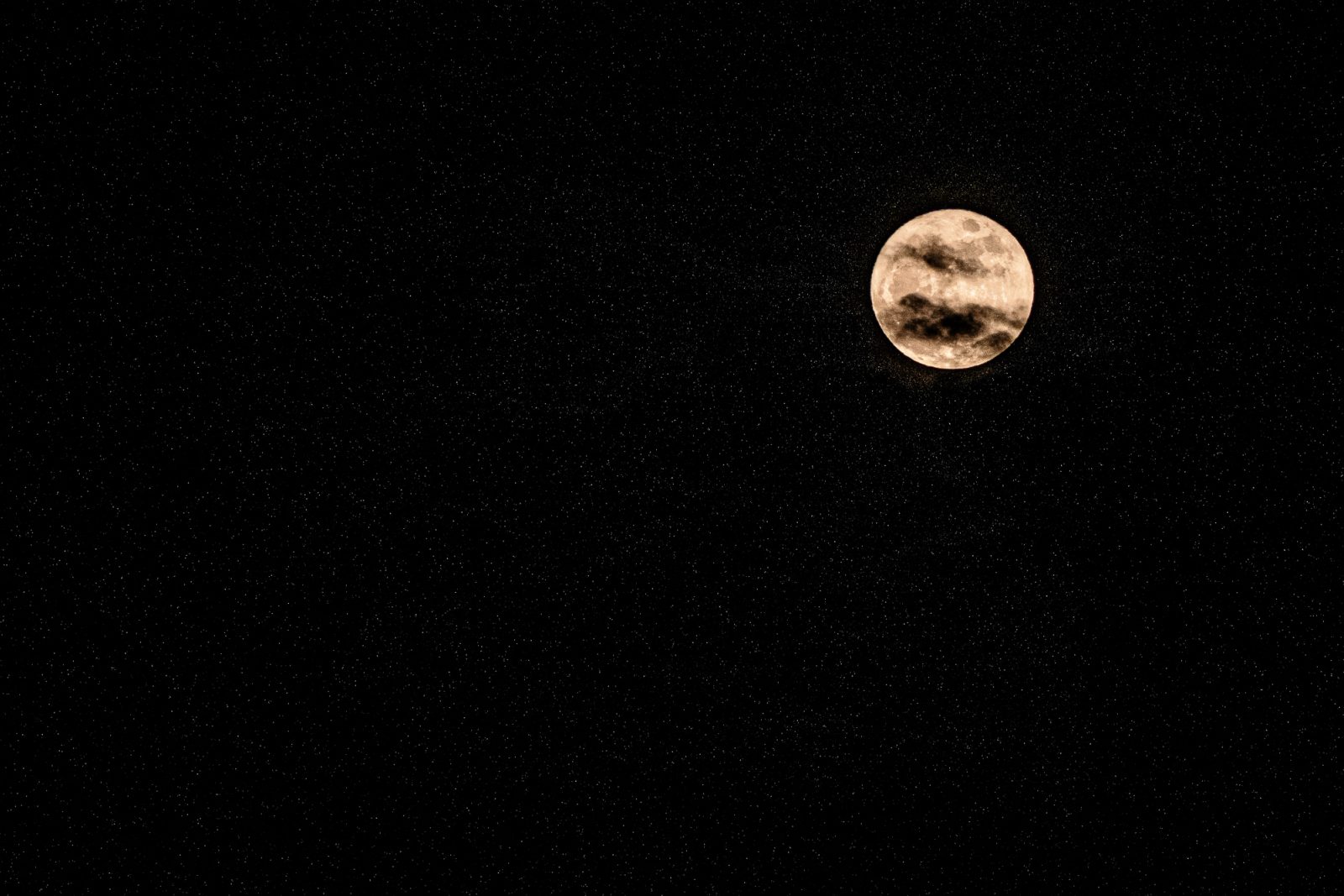 A full moon with visible surface details centered in a black night sky filled with scattered stars.