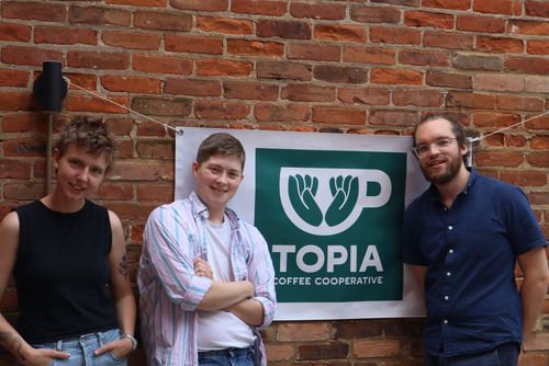 Topia Coffee Cooperative Team 3 members of Topia Coffee Cooperative stand in front of their company's logo