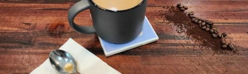 Coffee in a cup next to beans and a spoon on a table